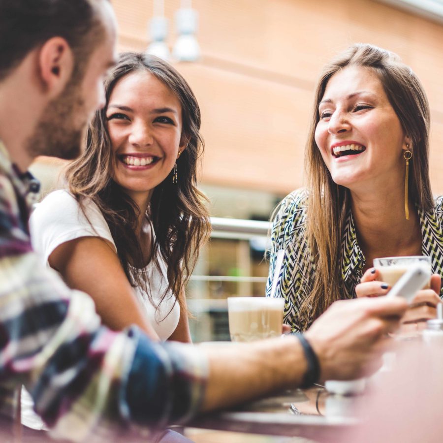 Two women drinking coffee and talking at the street. Young female friends smiling and have conversation outdoors.